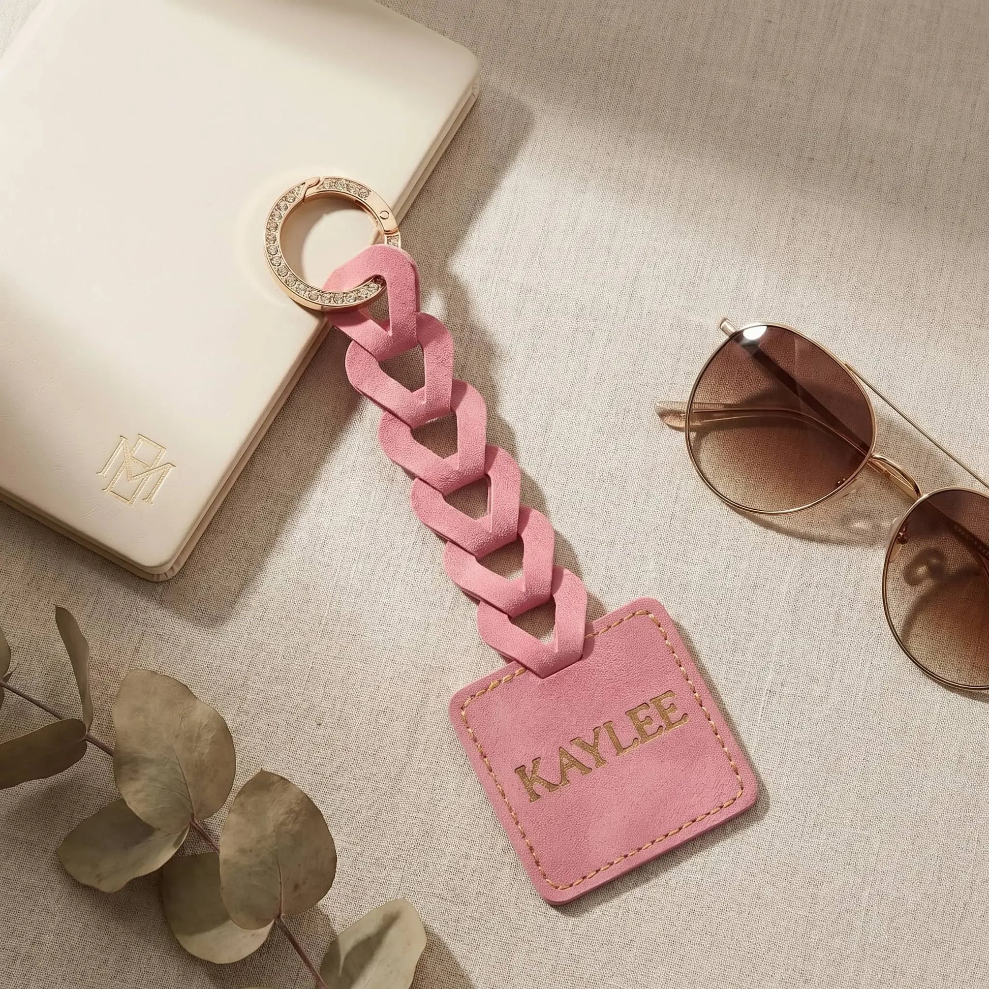 Pink Custom name tag on a neutral surface with sunglasses and leaves.