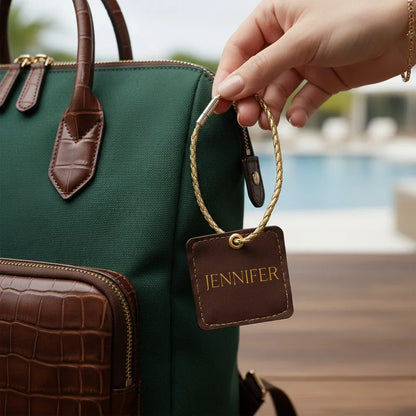 Green handbag with a brown leather tag labeled 'Jennifer' held by a hand.