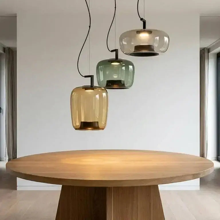 Danish glass pendant light with sculptural silhouettes in amber, green, and clear shades hanging above a wooden table.