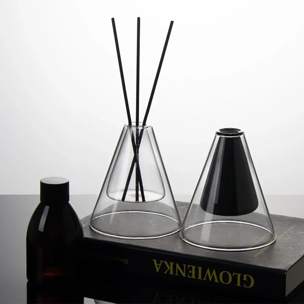 Diffuser with black sticks in a clear glass container on a dark surface.