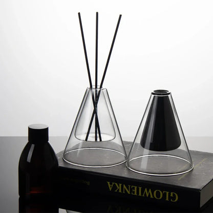 Diffuser with black sticks in a clear glass container on a dark surface.