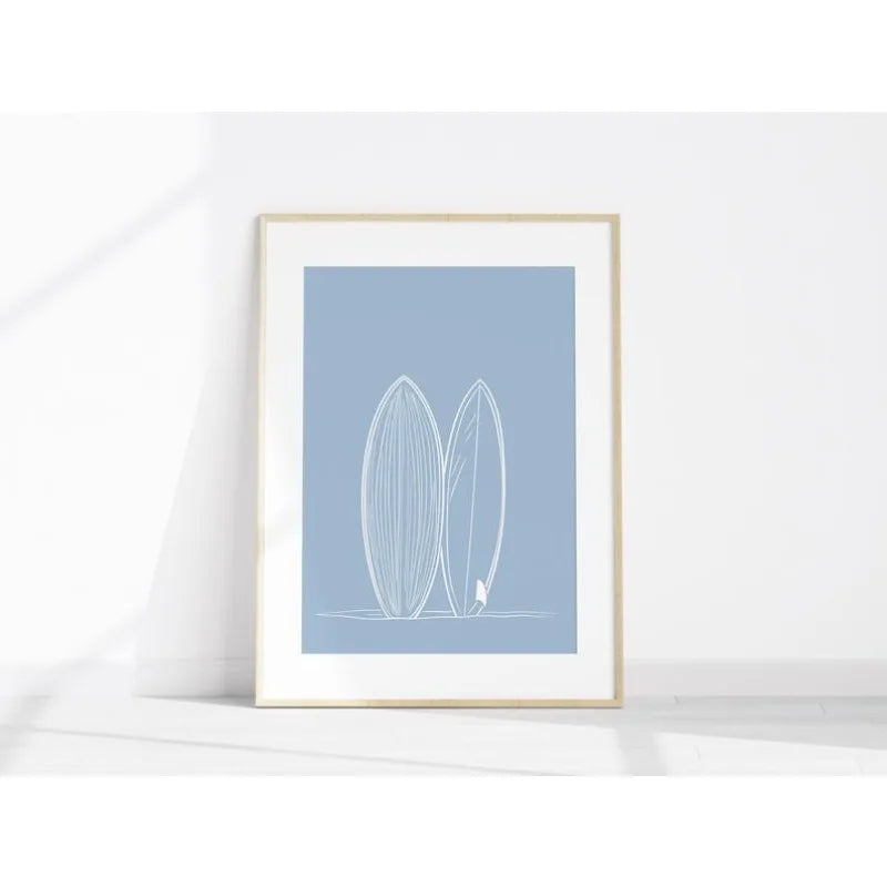 Framed artwork with two surfboards on a light blue background, displayed on a white surface.